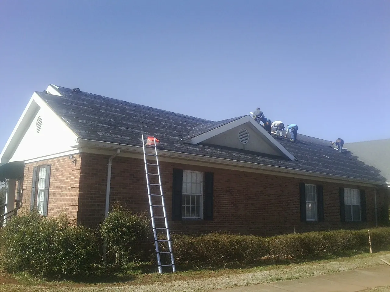 Crew tearing shingles off a brick ranch roof with a ladder set — Emergency Roof Repair work by our crew in Long Beach