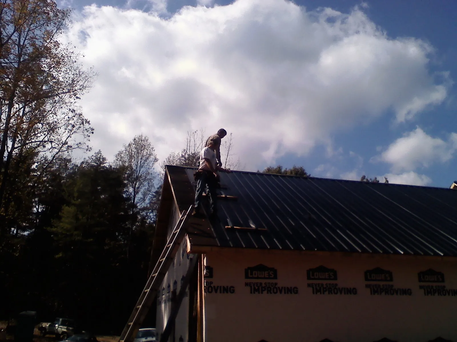 Roofer fastening dark metal panels high against a cloudy sky, from a Roof Inspection job in Long Beach