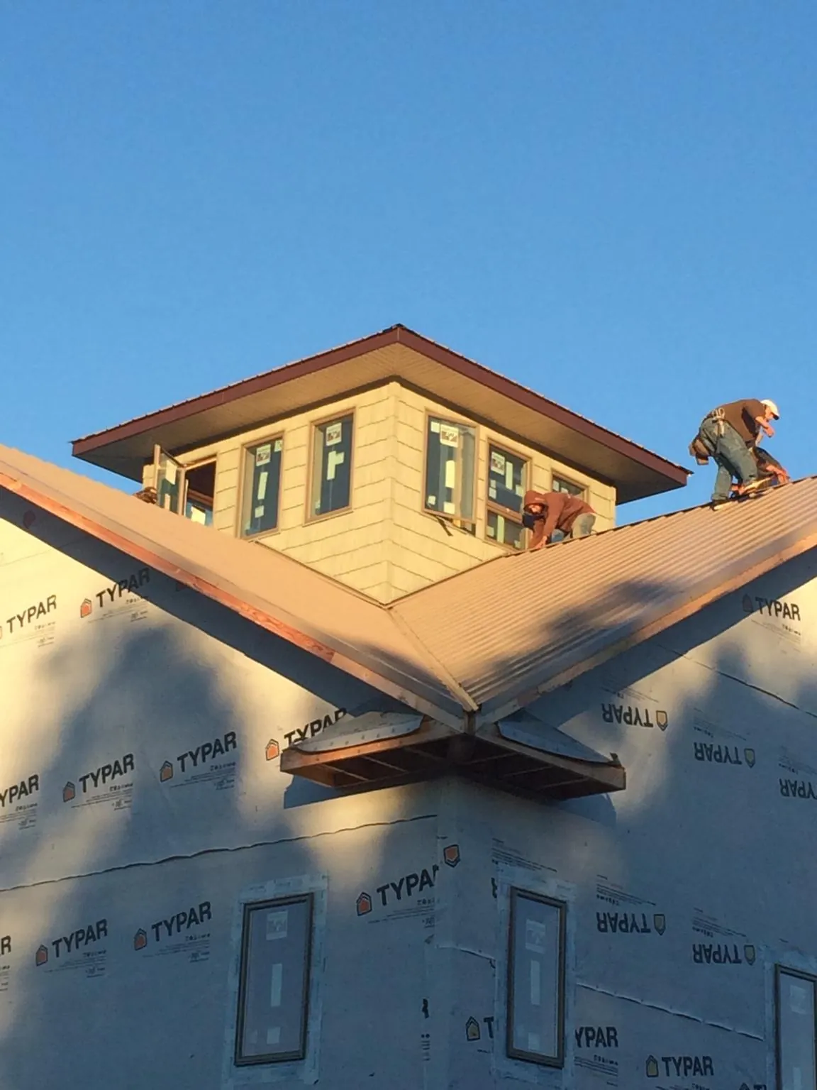 Roofers working around a rooftop cupola on a new metal roof at sunset — Roof Waterproofing in Long Beach by Roofing Brothers